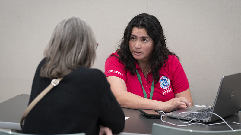 Female FEMA employee with brown hair and red shirt helps female resident with gray hair and black shirt at the Altadena Community Center.