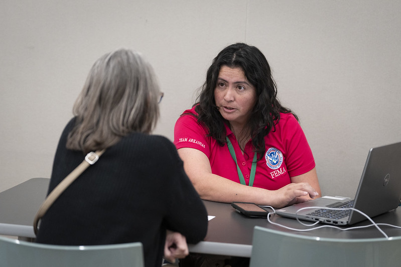 Female FEMA employee with brown hair and red shirt helps female resident with gray hair and black shirt at the Altadena Community Center.