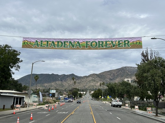 Banner reading "Altadena Forever" hangs above an Altadena street with mountains in the background.